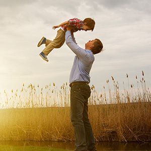 Happy father lifting his son in a beautiful field with sunset in the background